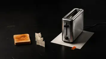 Smal brødrister i stål med en brødskive og en brettet målestrimmel